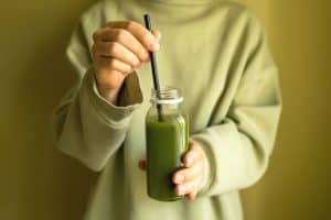 Fresh green juice in a glass bottle with a black straw, representing healthy lifestyle choices and wellness.
